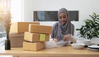 moslim bedrijfseigenaar vrouw die online winkelt, bereidt het productverpakkingsproces voor op kantoor, jong ondernemersconcept. foto