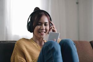 aantrekkelijke jonge vrouw op de bank thuis, ze speelt muziek met haar smarphone en draagt een koptelefoon, vrije tijd en entertainment concept foto