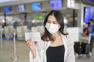 een reizigersvrouw draagt een beschermend masker op de internationale luchthaven, reist onder covid-19 pandemie, veiligheidsreizen, protocol voor sociale afstand, nieuw normaal reisconcept. foto
