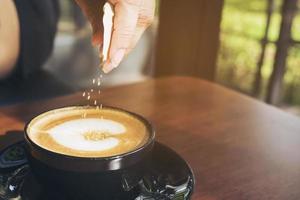 close-up van dame die suiker giet tijdens het bereiden van een warme koffiekop foto