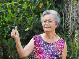senior vrouw staande glimlachend en duimen opdagen in de tuin foto
