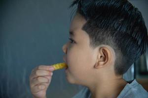 jongen die frietjesaardappel met gedimde saus eet over witte houten tafel foto