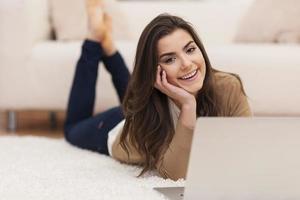 gelukkige vrouw liggend op tapijt met laptop foto