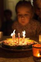 klein meisje blaast kaarsjes op de cake van de kindverjaardag foto