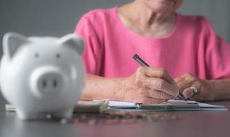 oude vrouw in roze shirt die aantekeningen maakt om pensioenfinanciën te plannen foto