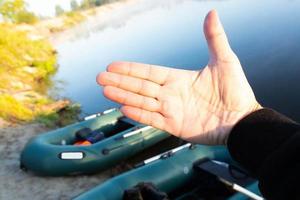 de palm van de hand van een man met een mazole van een riem tegen de achtergrond van twee rubberen opblaasbare boten met visgerei in de vroege ochtend, geparkeerd aan de oever van de rivier. foto