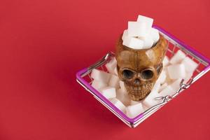 een mand gevuld met geraffineerde suikerklontjes met een menselijke schedel op een rode achtergrond. ruimte kopiëren. foto