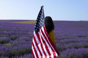 een jonge, donkerharige vrouw met de vlag van de verenigde staten van amerika tegen de zonnige hemel. herdenkingsdag en usa onafhankelijkheidsdag concept. foto