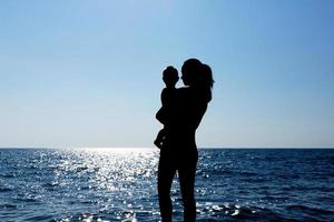 een jong meisje houdt een kind in haar armen tegen de zon. silhouet fotografie. foto