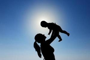 een jong meisje houdt een kind in haar armen tegen de zon. silhouet fotografie. foto