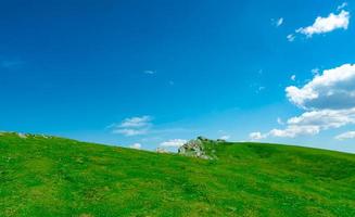 landschap van groen gras en rotsheuvel in het voorjaar met mooie blauwe lucht en witte wolken. platteland of landelijk uitzicht. natuur achtergrond in zonnige dag. frisse lucht omgeving. steen op de berg. foto