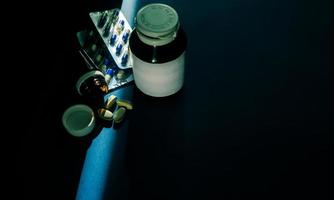 capsules en tabletten pillen met amberkleurige fles op donkerblauwe achtergrond met kopieerruimte. geneeskunde en supplementen interacties concept. drugsgebruik met een redelijk en wereldwijd gezondheidsconcept. foto