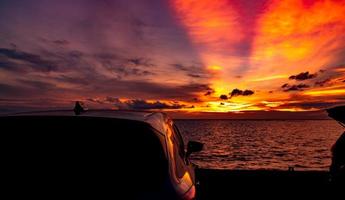 silhouet suv auto met sport en modern design geparkeerd op betonnen weg aan zee bij zonsondergang. road trip reizen op vakantie op het strand en open auto vrachtwagen met prachtige oranje zonsondergang hemel en wolken. foto