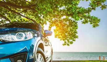 blauwe sport suv-auto geparkeerd door de tropische zee onder de parapluboom. zomervakantie aan het strand. zomer reizen met de auto. rondrit. auto-industrie. hybride en elektrisch autoconcept. zomerse sferen. foto