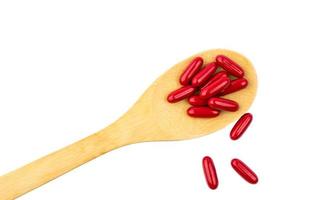 rode vitaminen en supplementen capsule op houten lepel geïsoleerd op een witte achtergrond met uitknippad en kopieer ruimte voor tekst. gebruik voor reclameontwerp over onderwerpen over gezondheidsinhoud foto