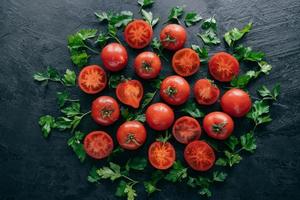 halve tomaten en groene peterselie rond op donkere achtergrond. verse ingrediënten voor het maken van vegetarische salade. geoogste tuingroenten foto