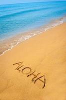 teken aloha geschreven in zand, op tropisch strand foto