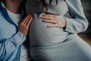 gezicht zwangere vrouw houdt handen op buik pose in de buurt van man wachten op kind. gelukkig familieconcept. zwangerschap en ouderschap concept foto