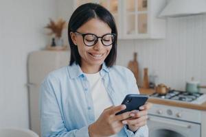 glimlachende vrouw gebruikt apps voor mobiele telefoons, bestelt boodschappen in de online winkel, controleert thuis sociale netwerken foto