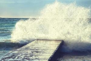 grote golven verpletterend op stenen pier, bij stormachtig weer. foto