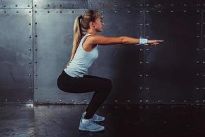 atletische jonge vrouw fitness model warming-up doen squats oefening foto