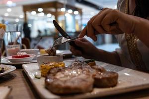 close-up gedeeltelijke weergave van vrouw geniet van het eten van biefstuk met vork en mes in restaurant foto