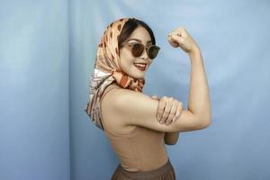 retro concept van een jonge Aziatische sterke vrouw die haar biceps toont geïsoleerd door een blauwe achtergrond foto