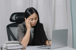 Aziatische vrouw moe tijdens het werken op laptop in haar kantoor. foto