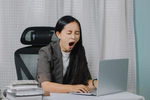 Aziatische vrouw geeuwen tijdens het werken op laptop in haar kantoor. foto