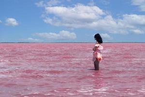 reiziger vrouw in roze jurk kijkt naar verbazingwekkende exotische roze zoutmeer en blauwe lucht. reislust reisconcept, kopieer ruimte voor tekst. foto