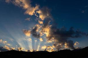 zonlichtstralen die door donkere wolken over bergen glanzen. foto