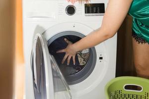 close-up van de hand van een vrouw die vuile kleren in de wasmachine stopt. foto