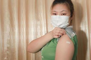 aziatische vrouw die een masker draagt, gips op haar arm toont na vaccinatie tegen covid-19, coronavirusvaccinatieconcept. foto