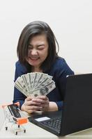 slimme vrouw in blauwe werkkleding houdt verschillende bankbiljetten vast in haar uitingen van vreugde. concept van het verkopen van merchandise of online zaken doen. foto