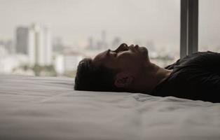 aziatische man voelt zich alleen verdrietig op bed met stadsachtergrond. blijf thuis, depressie en eenzaamheid concept. foto