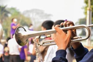 Aziatische jonge jongen student blaast een trompet met school marching band, wazige achtergrond foto