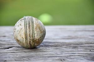 oude trainingscricket-sportuitrusting op donkere vloer, leren bal, wickets, helm en houten vleermuis, zachte en selectieve focus, traditionele cricketsportliefhebbers over de hele wereld. foto