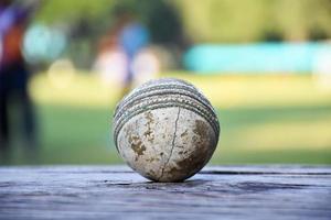 oude trainingscricket-sportuitrusting op donkere vloer, leren bal, wickets, helm en houten vleermuis, zachte en selectieve focus, traditionele cricketsportliefhebbers over de hele wereld. foto