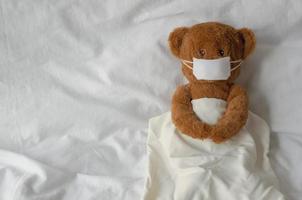 teddybeer speelgoed dragen masker slaap op bed. blijf thuis weg van het virusconcept. foto