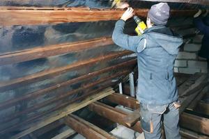 de tovenaar gebruikt een accuboormachine en schroeft de schroeven in planken die folie en minerale wol bevatten om het dak van het huis te genezen foto