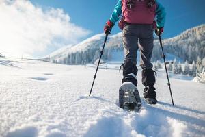 een vrouw met een rugzak op sneeuwschoenen beklimt een besneeuwde berg foto