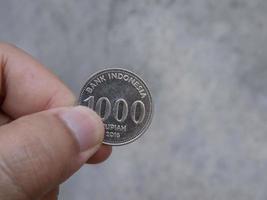 een man met een munt van 1000 rupiah in Indonesische valuta op een wazige grijze achtergrond foto