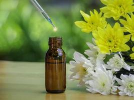 het extract van etherische oliën en medische bloemenkruiden in de buurt van de witte en gele bloem op houten tafel. de etherische olie biologische bio alternatieve geneeskunde, bruine fles. foto