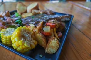 gegrilde biefstuk met jus wordt geserveerd met een groente- en fruitsalade in een zwarte keramische plaat op de eettafel om de biefstuk voor te bereiden op een feestelijk diner. foto