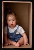 gelukkig klein meisje zit in een kartonnen doos en heeft plezier foto