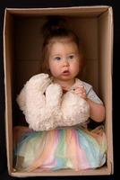 gelukkig klein meisje zit in een kartonnen doos en heeft plezier foto
