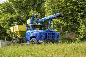 oude blauwe en gele vrachtwagenmachines geparkeerd op gras tegen bomen in de oude stad foto