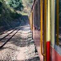 speelgoedtrein die zich op berghellingen beweegt, prachtig uitzicht, een zijberg, een zijvallei die zich op een spoorlijn naar de heuvel beweegt, tussen groen natuurlijk bos. speelgoedtrein van kalka naar shimla in india foto