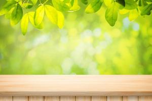houten tafelvloer en mooi natuurlijk groen blad abstract wazig bokeh lichte achtergrond foto