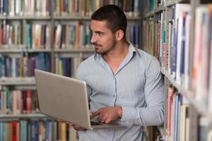 jonge student met behulp van zijn laptop in een bibliotheek